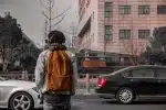 man in orange and black jacket standing on sidewalk during daytime