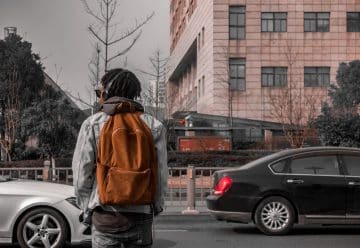man in orange and black jacket standing on sidewalk during daytime