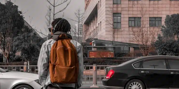 man in orange and black jacket standing on sidewalk during daytime