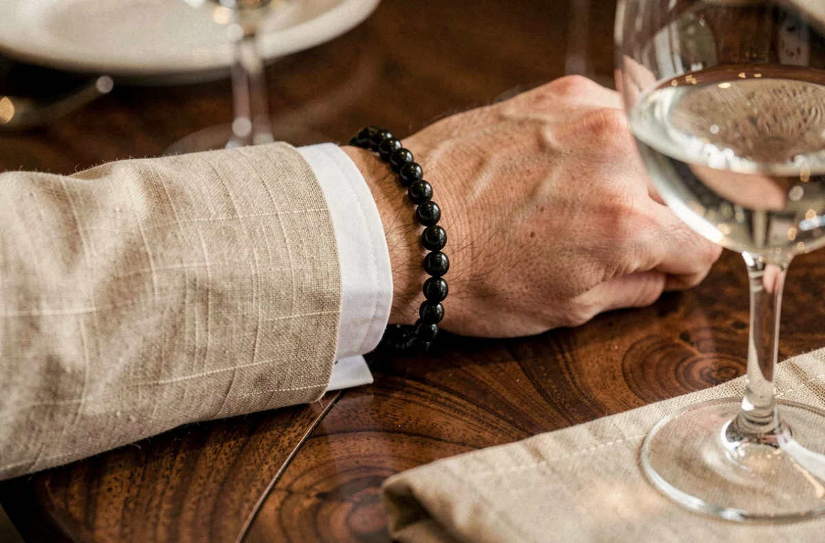 Gros plan d'un bracelet de perles noires de Tahiti porté avec un costume en lin beige sur une table en bois dans un restaurant élégant